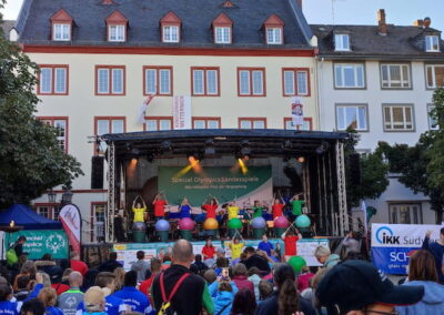 Menschenmenge auf einem Platz bei den Special Olympics Landesspielen vor einer Bühne, auf der Künstler auftreten, umgeben von historischen Gebäuden.