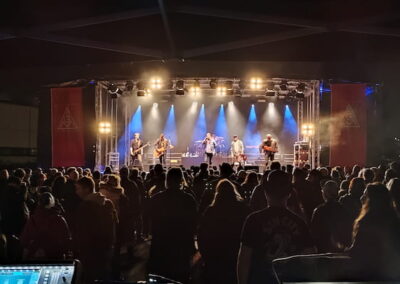 Menschenmenge bei einem Open-Air-Konzert in der Nacht, beobachten eine Band auf einer beleuchteten Bühne.