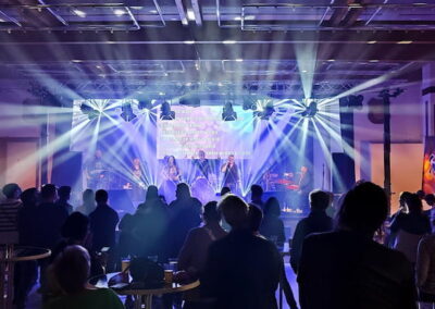 Publikum steht und beobachtet eine Live-Band auf einer Bühne, die durch dramatische blaue und weiße Lichtstrahlen beleuchtet wird, während Banner mit der Aufschrift "Soul Mates" im Hintergrund hängen.