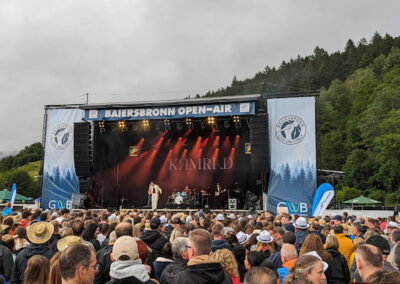 Menschenmenge bei einem Open-Air Konzert in Baiersbronn, vor einer Bühne mit Band, umgeben von bewaldeten Hügeln.