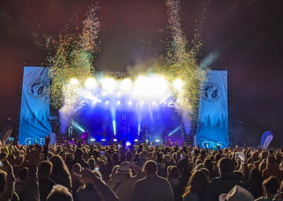 Menschenmenge bei einem Open-Air-Musikfestival bei Nacht, beobachten eine Bühnenshow mit leuchtenden Scheinwerfern und Feuerwerk.